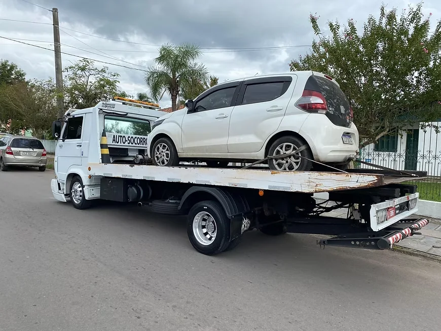 Carro hatch branco sendo transportado em rua residencial de Santa Maria