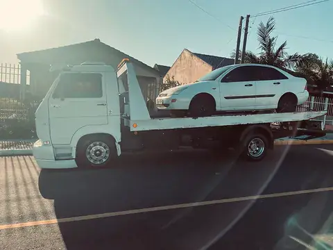 Carro sedan branco sobre a plataforma do guincho em dia ensolarado