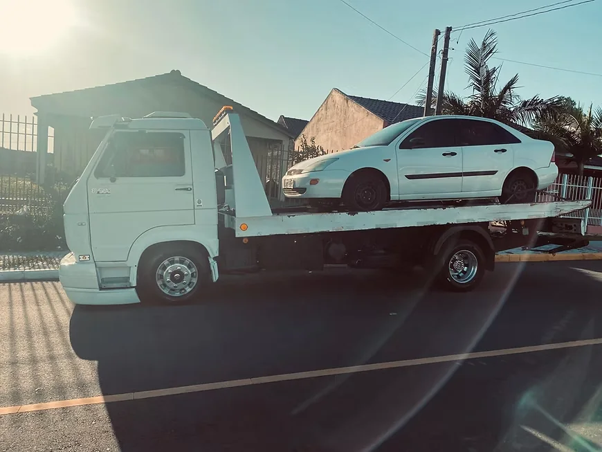 Carro sedan branco sobre a plataforma do guincho em dia ensolarado